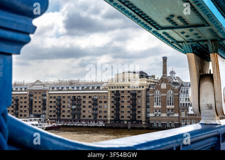 London, England – 14. Juli 2026: Historische Lagerhäuser von Butler's Wharf und die Themse, gesehen durch die blaue Stahlkonstruktion der Tower Bridge Stockfoto