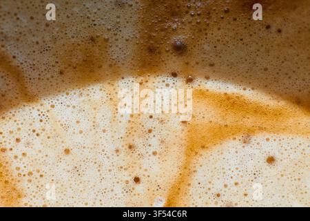 Makro-Nahaufnahme, die die reiche Textur und die zarten Bläschen von frisch gebrühtem Kaffee-Crema zeigt und ein warmes abstraktes Hintergrundmuster erzeugt. Stockfoto