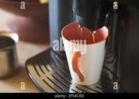 Nahaufnahme einer automatischen Kaffeemaschine, die frisch gebrühten heißen Espresso in eine Keramiktasse auf einer Küchentheke am Morgen ausschenkt Stockfoto