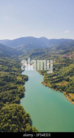 Vertikale Luftansicht des smaragdgrünen Plastiras-Sees, der durch dichte grüne Kiefernwälder bedeckte Berge in Thessalien, Griechenland, für Naturreise-Stockmaterial Stockfoto