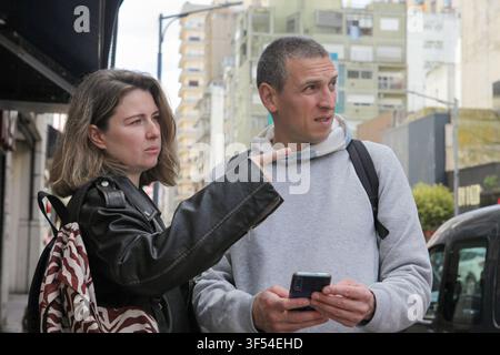 Mitte-alterliches Paar überprüft Informationen auf einem Smartphone zusammen, während es eine Straße in der Stadt entlanggeht. Stockfoto