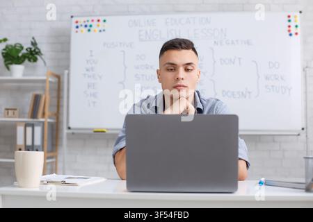 Übe Englisch mit Tutor remote während der COVID-19-Epidemie. Konzentrierter junger männlicher Lehrer hört Student online zu und schaut auf Laptop im Wohnzimmer Stockfoto