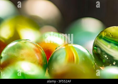 Glasmurmel in grünen, gelben und orangefarbenen Tönen, die einen abstrakten Hintergrund mit unscharfen Bokeh-Lichtern bilden Stockfoto