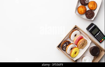 Take Away, Lieferung und Fast Food. Donuts mit Glasur und Krume, Muffins und Kaffee in Pappbechern und kontaktlosem Terminal Stockfoto