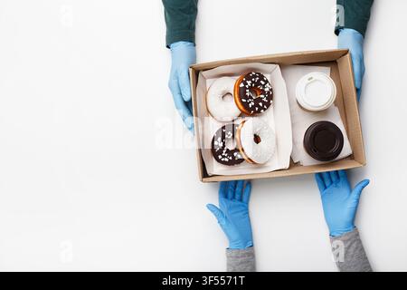 Kellner gibt Bestellung während der Coronavirus-Epidemie und schnellem Kundenservice auf. Kunde nimmt Kiste mit Donuts mit weißer und schokoladenüberzogener Glasur und Krümel und zwei Stockfoto
