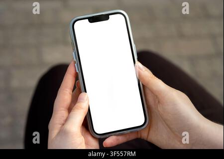 Frau hält ein modernes Smartphone mit leerem weißem Bildschirm-Mockup in den Händen im Freien Stockfoto
