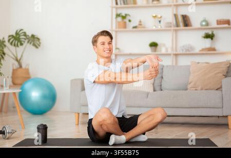 Heimsport, um fit zu bleiben. Lächelnder Mann, der die Handübungen macht, sitzt in Lotushaltung auf der Matte Stockfoto