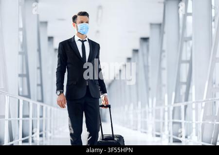 Hübscher junger Geschäftsmann in Schutzmaske, der am Flughafen läuft Stockfoto