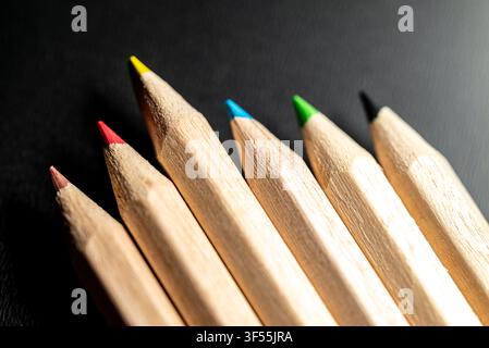 Nahaufnahme-Makroaufnahme von scharfen farbigen Holzbuntstiften, die diagonal auf einem dunklen schwarzen Hintergrund aufgereiht sind Stockfoto