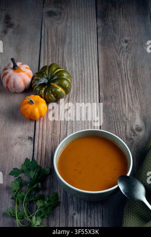 Oberansicht einer Schale mit Kürbiskremesuppe, silbernem Löffel, dekorativen Kürbissen und grünem Tuch auf rustikaler Holzoberfläche mit Kopierraum Stockfoto