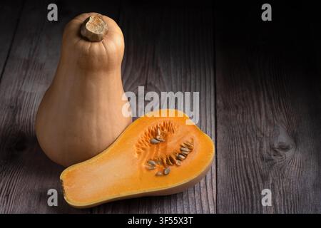 Frischer Butternusskürbis ganz und halbiert mit Samen auf rustikalem dunklem Holzuntergrund mit Kopierraum Stockfoto