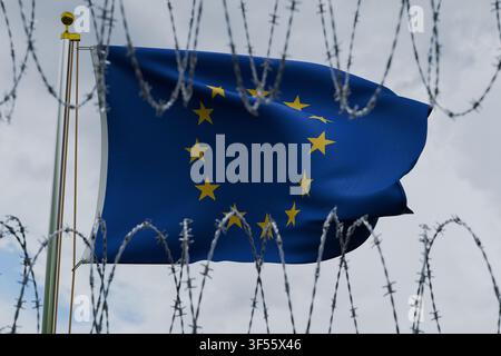Die Flagge der Europäischen Union weht an einer Fahnenstange, gesehen hinter scharfem Stacheldraht vor einem bewölkten Himmel. Konzeptbild, das EU-Einwanderung darstellt Stockfoto