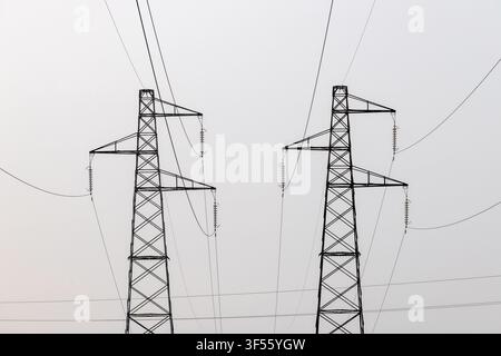 Nahaufnahme von zwei Hochspannungsmasten und Stromkabeln vor einem minimalen klaren Himmelshintergrund. Stockfoto