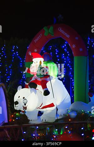 aufblasbarer Weihnachtsmann reitet auf Eisbären bei einer Weihnachtsausstellung im Freien mit festlichen Lichtern und Dekorationen in weiß, rot, grün und blau, fröhlich und f Stockfoto