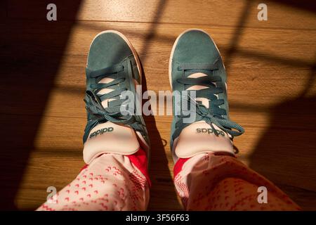 Tyumen, Russland-10. April 2026: Von oben nach unten auf einer Person, die neue Adidas-Sneakers in Teal auf Holzboden trägt Stockfoto