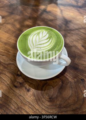 Hohe Blickwinkelansicht einer Tasse Matcha-Green-Tea-Latte auf einem holzmaserierten Tisch Stockfoto