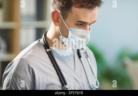 Nahaufnahmeporträt eines nachdenklichen Mannes, Arzt oder Krankenschwester, mit blauer Gesichtsmaske in einer medizinischen Klinik Stockfoto