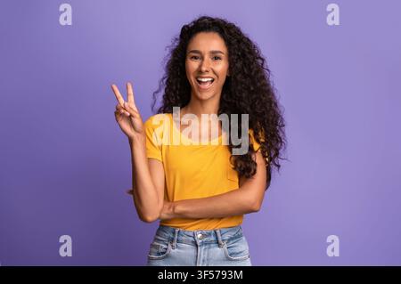 Fröhliche Junge Frau Gestikulierend Frieden, Spaß Beim Posieren Über Lila Hintergrund Stockfoto