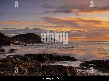 Mumbles-Leuchtturm als Silhouette auf felsiger Landzunge bei Sonnenaufgang, dramatischer orangefarbener und goldener Himmel, Wellen brechen über Felsen im Vordergrund, Gower-Halbinsel, Wales Stockfoto