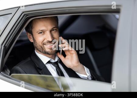 Fröhlicher Unternehmer, der während der Fahrt mit dem Auto telefoniert Stockfoto