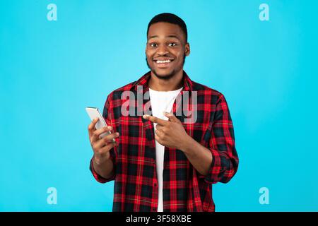 African Guy Zeigt Finger Auf Smartphone Stehen Über Blauen Hintergrund Stockfoto