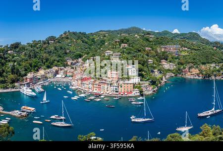 Panoramablick auf das wunderschöne Portofino an einem Frühlingsnachmittag mit Hafen, Booten, Yachten, Uferpromenade, Villen, grüne Hügel und klares blaues Wasser an der ligurischen Küste in Italien vor blauem Himmel Stockfoto
