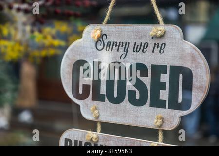 Ein rustikales Holzschild mit dem Text Sorry we are closed hängt an einer Ladentür mit verschwommenem Hintergrund. Stockfoto