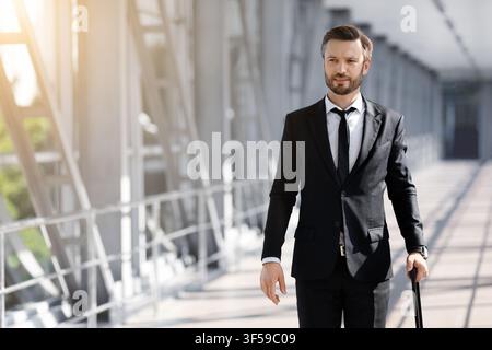 Wohlhabender Geschäftsmann mit Gepäck, der am Flughafen vorbei läuft Stockfoto