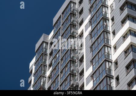 Höheres Wohngebäude präsentiert eine Fassade aus glänzendem Glas und weißen Paneeln, die den lebendigen blauen Himmel darüber reflektieren und das zeitgenössische Design hervorheben Stockfoto
