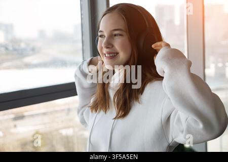 Junge Frau genießt Musik mit Kopfhörern und schaut aus dem Fenster Stockfoto