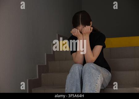 Frau, die eine Depression erlebt, sitzt auf der Treppe und bedeckt ihr Gesicht Stockfoto