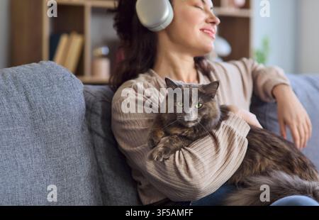 Nahaufnahme einer Frau mit Katze, die auf dem Sofa entspannt und Musik über Kopfhörer hört Stockfoto