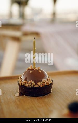Einziger Schokoladen-Mousse-Kuchen mit einer goldenen Kerze oben drauf, arrangiert für eine Geburtstagsfeier. Die Szene betont ein festliches Dessert mit einer warmen und eleganten Atmosphäre Stockfoto