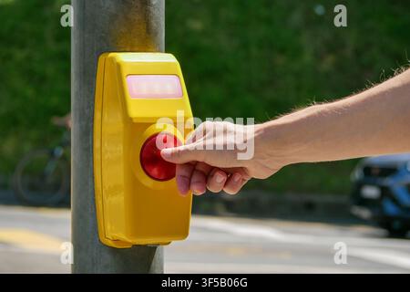 Hand, die den roten Fußgängerüberquerungs-Knopf auf einer gelben Signalbox drückt – Konzept für städtische Sicherheit, Barrierefreiheit und Verkehrskontrolle Stockfoto