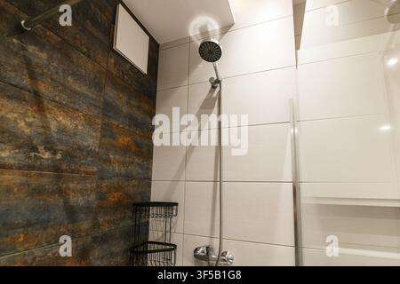 Modernes Badezimmer-Interieur mit Kontrast zwischen dunklen, texturierten Steinwänden und weißen glänzenden Fliesen. Luxuriöses minimalistisches Toilettendesign, zeitgenössische Architektur, Premium-Wohnungsrenovierung Stockfoto