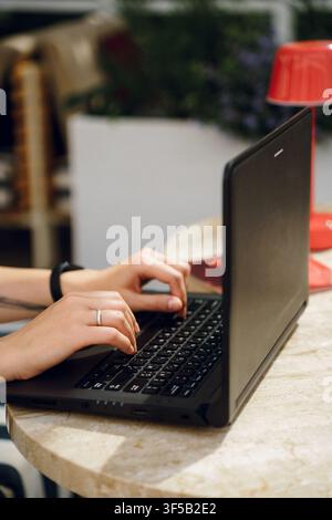 Frau, die im Freien an einem Laptop tippt, repräsentiert Fernarbeit und Freelancing-Lebensstil. Natürliches Licht und entspannte Umgebung betonen Flexibilität und modernen Arbeitsstil Stockfoto