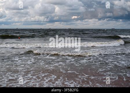 Stürmische See mit schaumigen Wellen an einem sandigen Strand unter einem dunklen bewölkten Himmel. Konzept von rauem Ozeanwetter, Küstenlandschaft, Wellenbewegung, kräftigen Gezeiten und stimmungsvoller Meereslandschaft Stockfoto