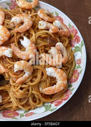 Spaghetti mit Garnelen in Tomatensauce, serviert auf einem Blumenmuster-Teller auf Holztablett, Nahaufnahme Stockfoto