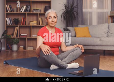 Senior Caucasian Woman praktiziert Yoga zu Hause, konzentriert auf Meditation, Wellness-Konzept Stockfoto