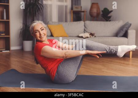 Zufriedene Seniorin trainiert zu Hause auf der Matte, macht Pilates, Wellness-Konzept Stockfoto