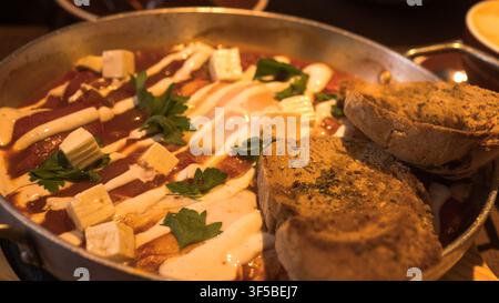 Shakshuka in einer Pfanne mit Fetakäse, Joghurt-Drizzle und geröstetem, gekörntem Brot — Konzept: Mittleröstliches Frühstück, Komfortessen, Restaurantessen, Stockfoto