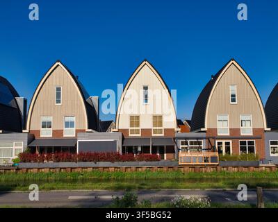 Niederlande - 18. Apr 2026: Zeitgenössische gewölbte Häuser entlang einer Uferstraße in den Niederlanden leuchten im warmen Abendlicht unter einem klaren blauen Himmel Stockfoto