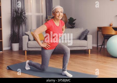 Zufriedene Seniorin macht Lunges zu Hause, gesundes Fitnesskonzept Stockfoto