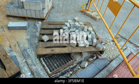 Bordsteine sind auf einer Holzpalette neben einem Baustellenbereich gestapelt. Eine Absperrung ist sichtbar, die auf laufende Straßenreparaturen hinweist. Kies und Erde su Stockfoto