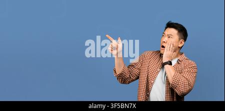 Überraschter asiatischer Mann, der mit der Hand auf das Gesicht zeigt und Schock ausdrückt, blauer Hintergrund Stockfoto