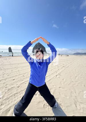 Frau, die verspielt am Sandstrand in der Nähe von Haystack Rock in Cannon Beach, Oregon, USA, posiert. Stockfoto