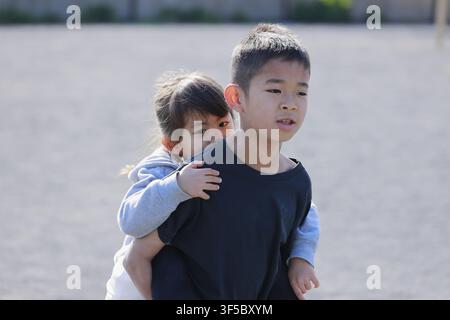 Japanischer Junge trägt seine Schwester auf dem Rücken (10-jähriger Junge und 5-jähriges Mädchen) Stockfoto