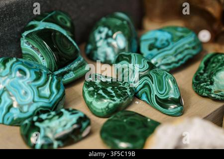 Gruppe von polierten grünen Malachitsteinen mit natürlichen Banderungsmustern auf einer weichen hellbraunen Oberfläche. Lebendige smaragdgrüne Kupferkarbonatmineralien, Edelsteinpolierung, Steinsammeln Stockfoto