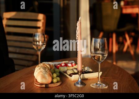 Romantisches Abendessen-Tisch-Setup mit Weingläsern, Kerzenlicht und frischem Brot auf einem Holztisch bei Sonnenuntergang. Intime Golden-Hour-Date-Nacht, rustikales Outdoor-Esserlebnis Stockfoto