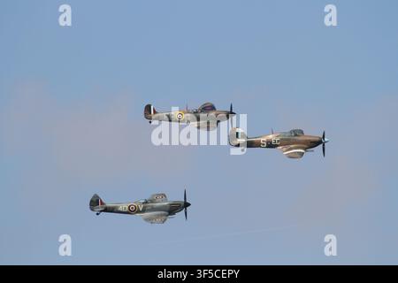 Drei alte Jagdflugzeuge aus dem Zweiten Weltkrieg, darunter zwei Supermarine Spitfires und eine Hawker Hurricane, fliegen in Formation vor einem klaren blauen Himmel. Stockfoto